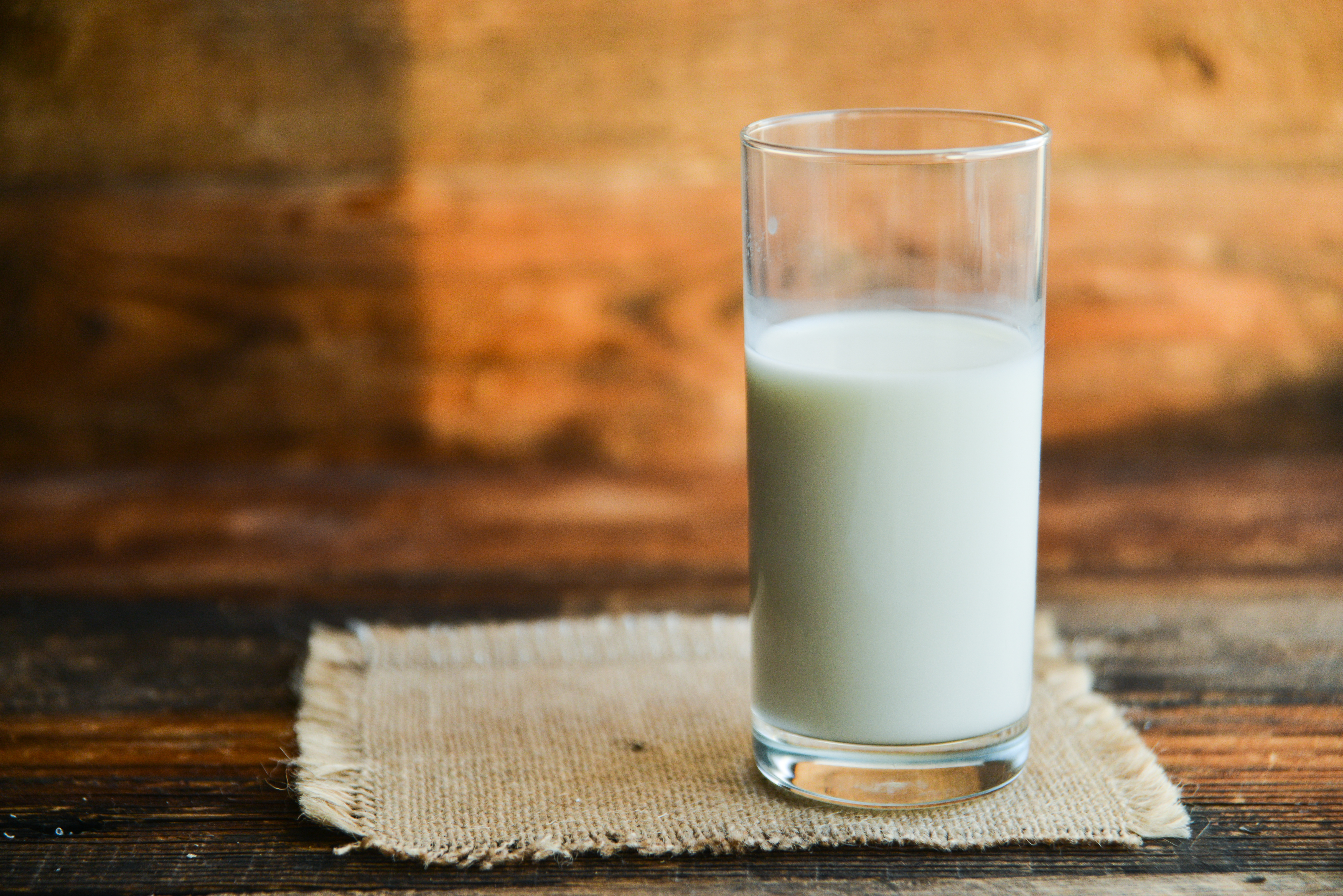 A glass of milk ready to drink placed on a jute napkin on a wooden table.