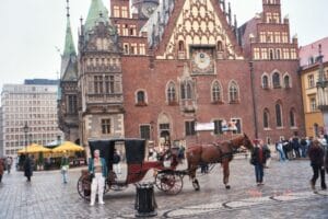 The outside of an older-style building, with a horse-drawn carriage in front of it.