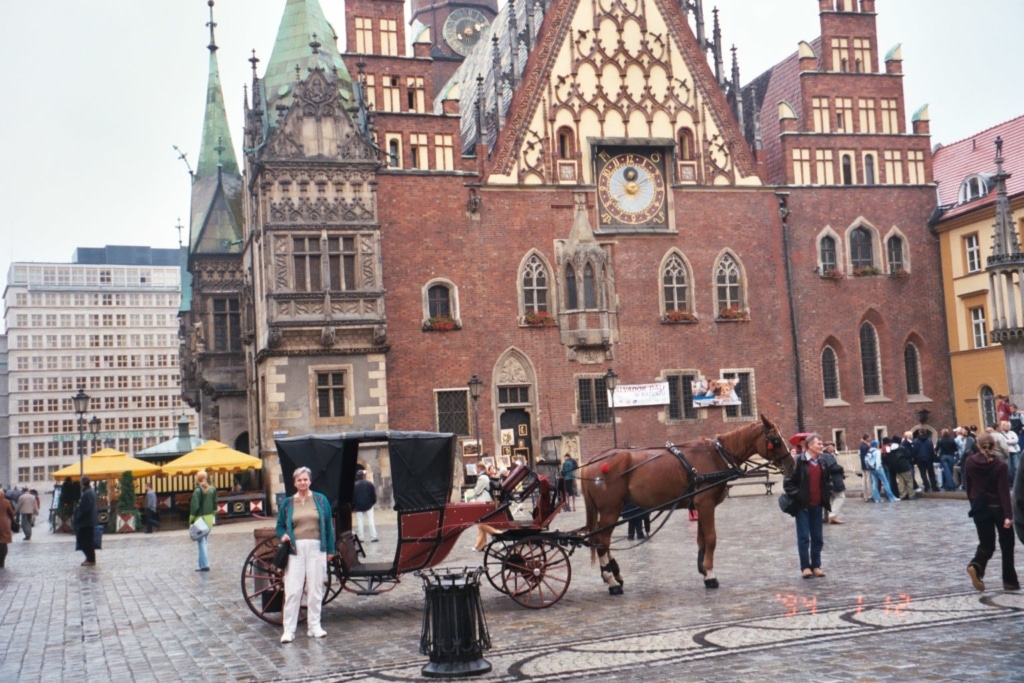 0300501133898319900620084938147-1024×683 The outside of an older-style building, with a horse-drawn carriage in front of it.