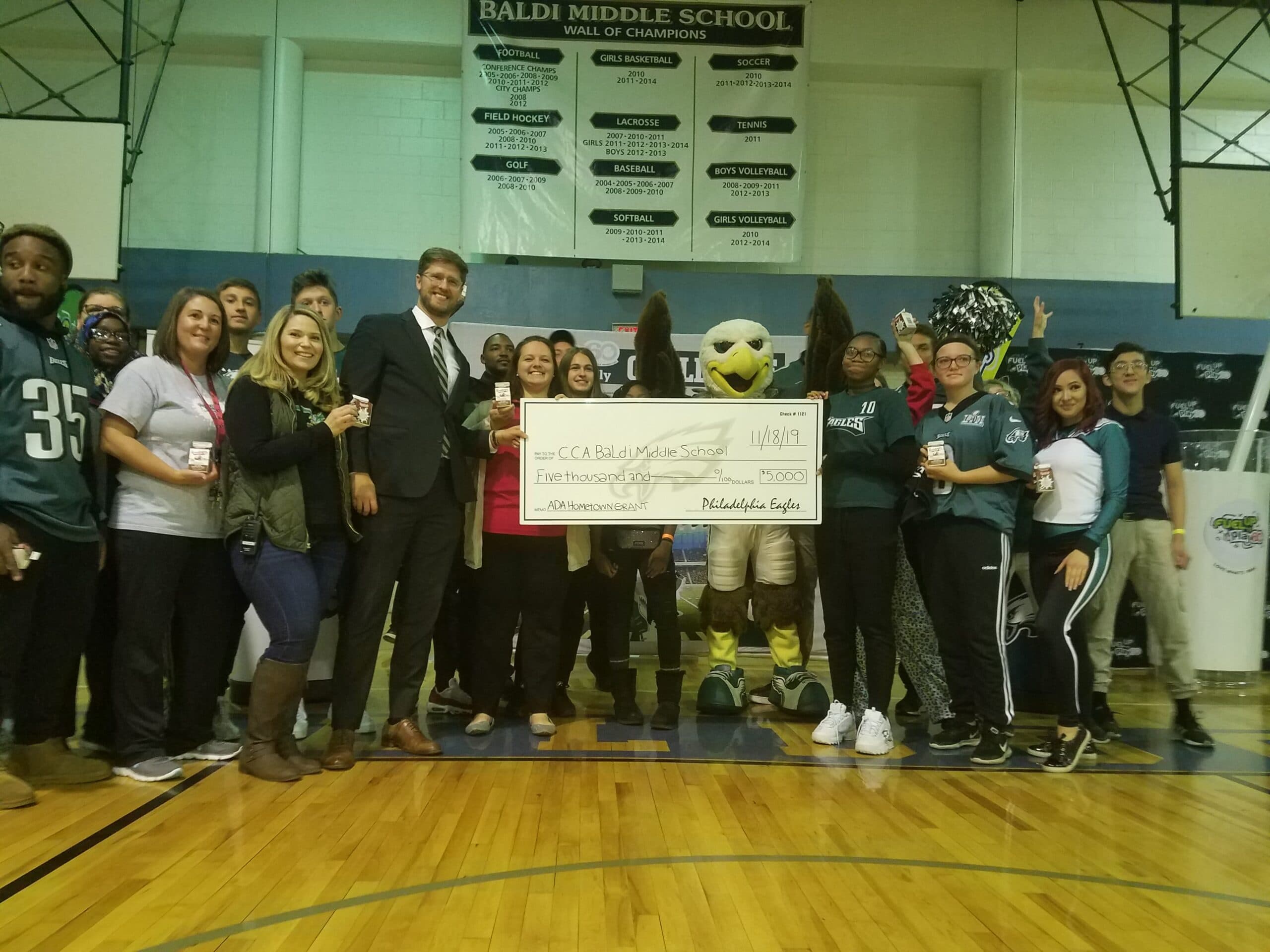 group of students in a school gym with a big check