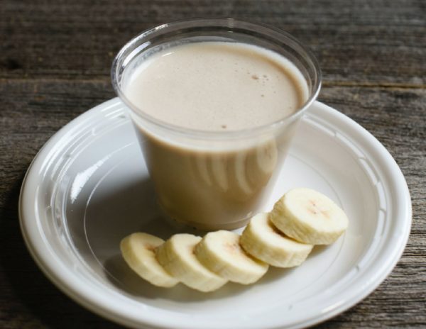 A chunky monkey smoothie made of peanut butter and banana served in a cup next to banana slices.