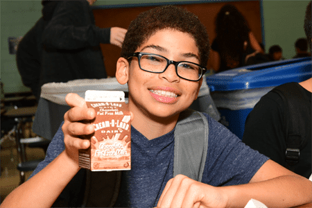 A smiling kid holding a carton of chocolate milk.