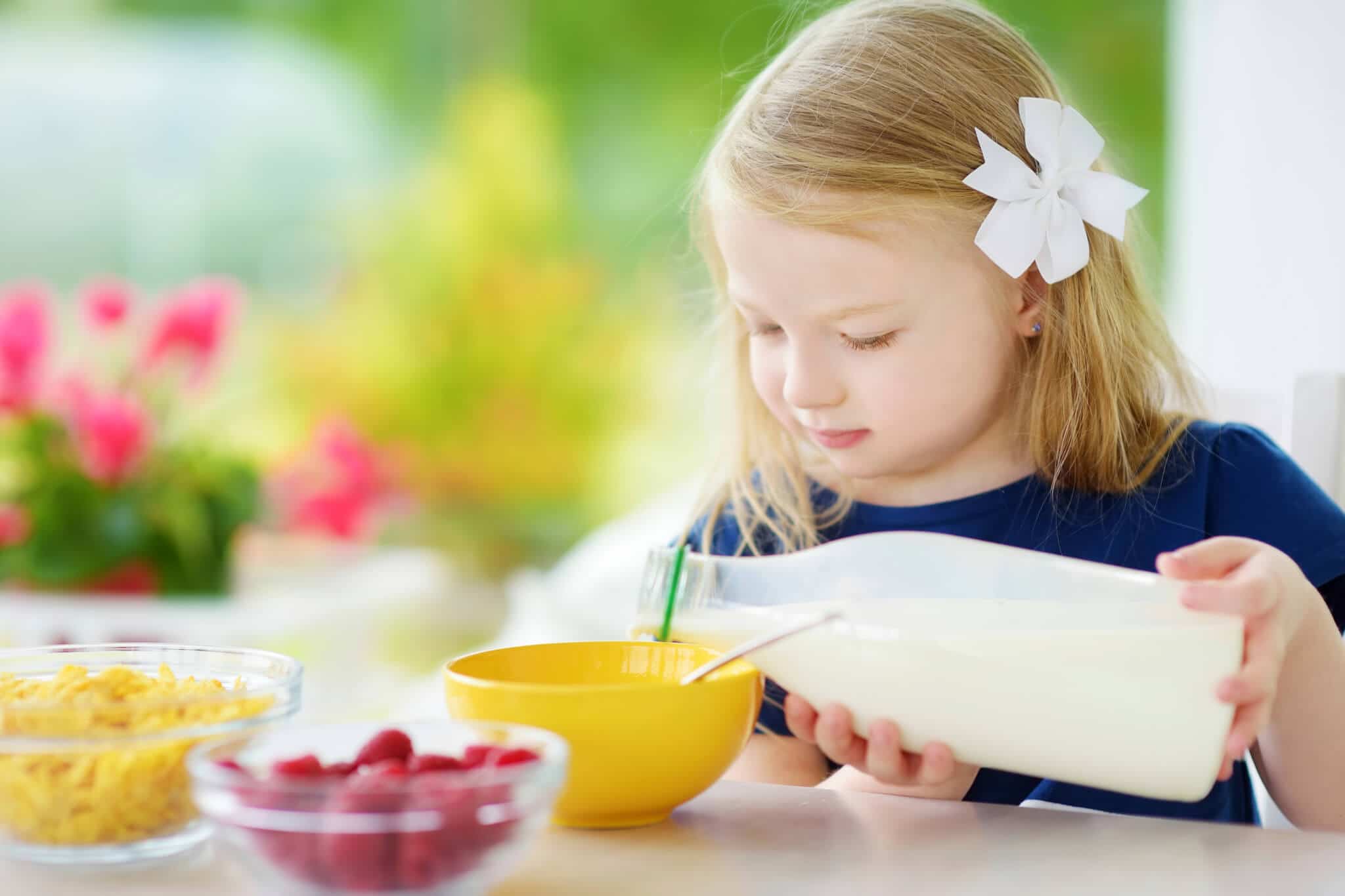 Young girl pouring milk in bowl.