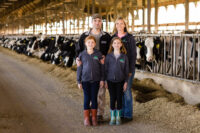 LAMB FARMS 2020_010 Family posing in front of a line of cows