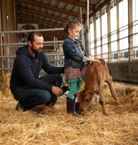 Man helping a little girl pet a calf