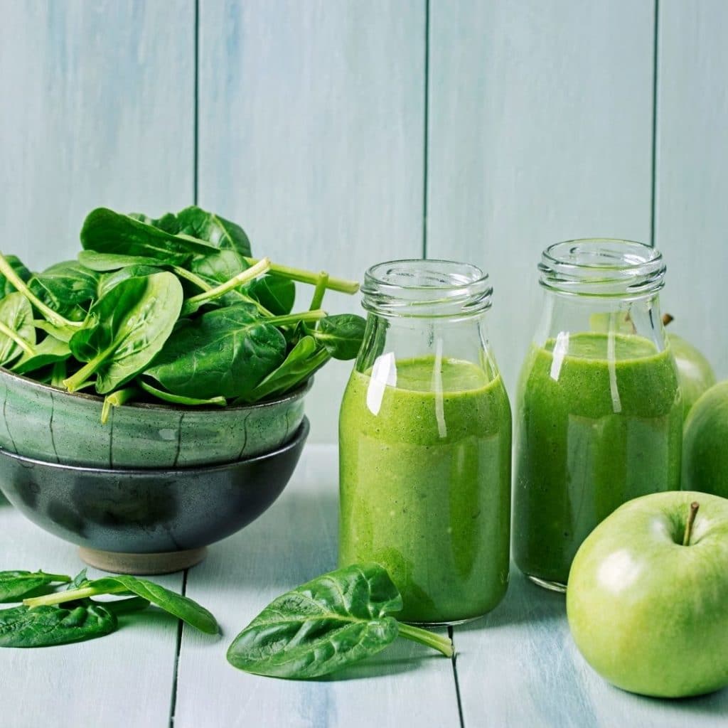 Glasses of green smoothies with leaves and apple