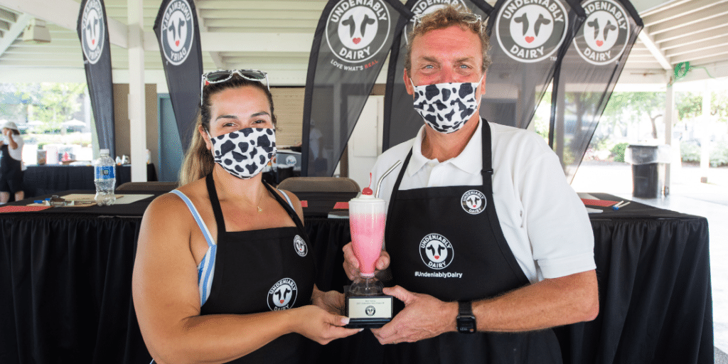 A couple wearing masks holding up a milkshake glass with a straw as a reward.