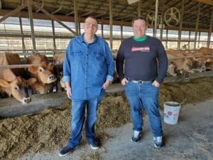 Two men standing in a barn with cows behind them
