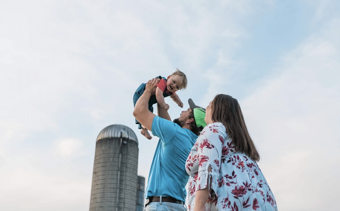 parents holding a baby up next to a farm silo