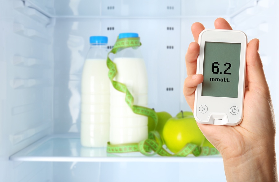 Male hand holding glucometer with food on shelf of refrigerator
