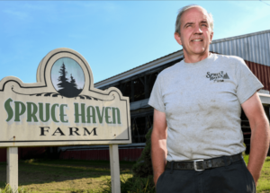 Man standing next to a Spruce Haven Farm sign