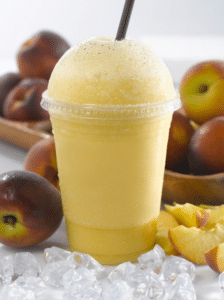A peach smoothie served in a cup with ice cubes around it.