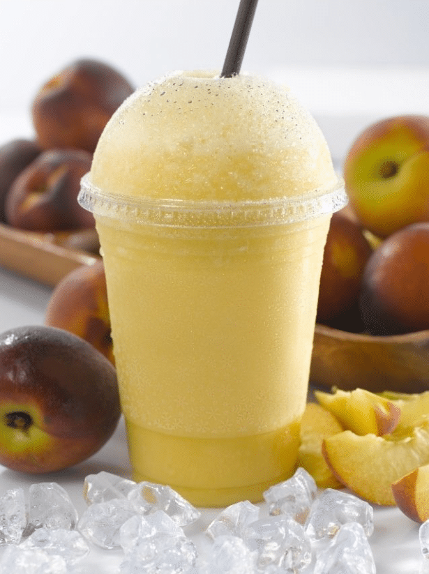 A peach smoothie served in a cup with ice cubes around it.