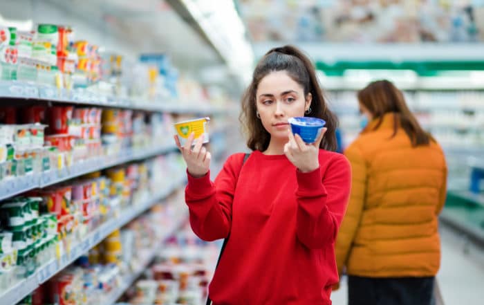 A woman compares two different packages of yogurt in a supermarket.