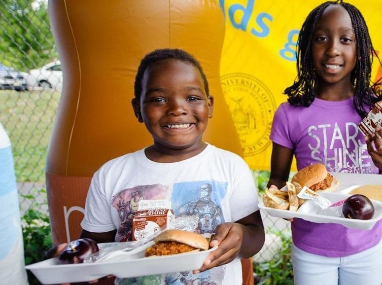 Two children smiling while they each hold a platter of food.