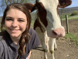 The selfie of a dairy farmer smiling next to a cow.