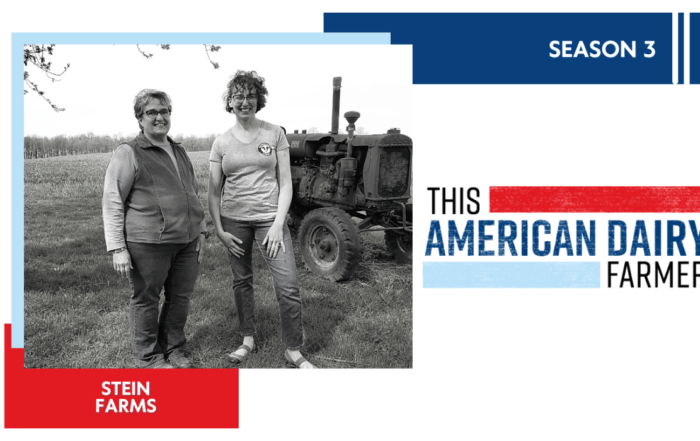 Two female dairy farmers stand in a field beside a tractor at Stein Farms.