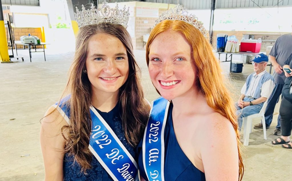 Two Dairy Princesses posing together, adorned with crowns and blue sashes.