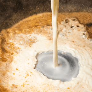 A frying pan being filled with cheese and milk sauce to make butternut squash pasta.