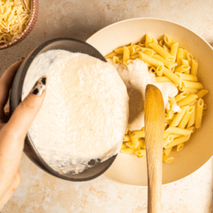 A woman's hand filling a ceramic bowl with cooked pasta and butternut squash pasta sauce.