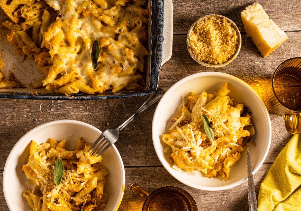 Two ceramic bowls filled with butternut squash pasta, accompanied by a small bowl filled with shredded cheese.