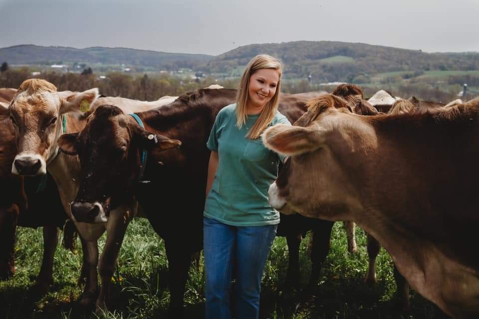 A young dairy farmer surrounded by dairy cows in a field.