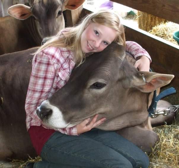 A young female dairy farmer hugging a dairy cow.