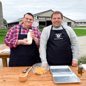 Farmer and chef showcasing a glass bottle of milk, surrounded by cooking supplies on a wooden table.