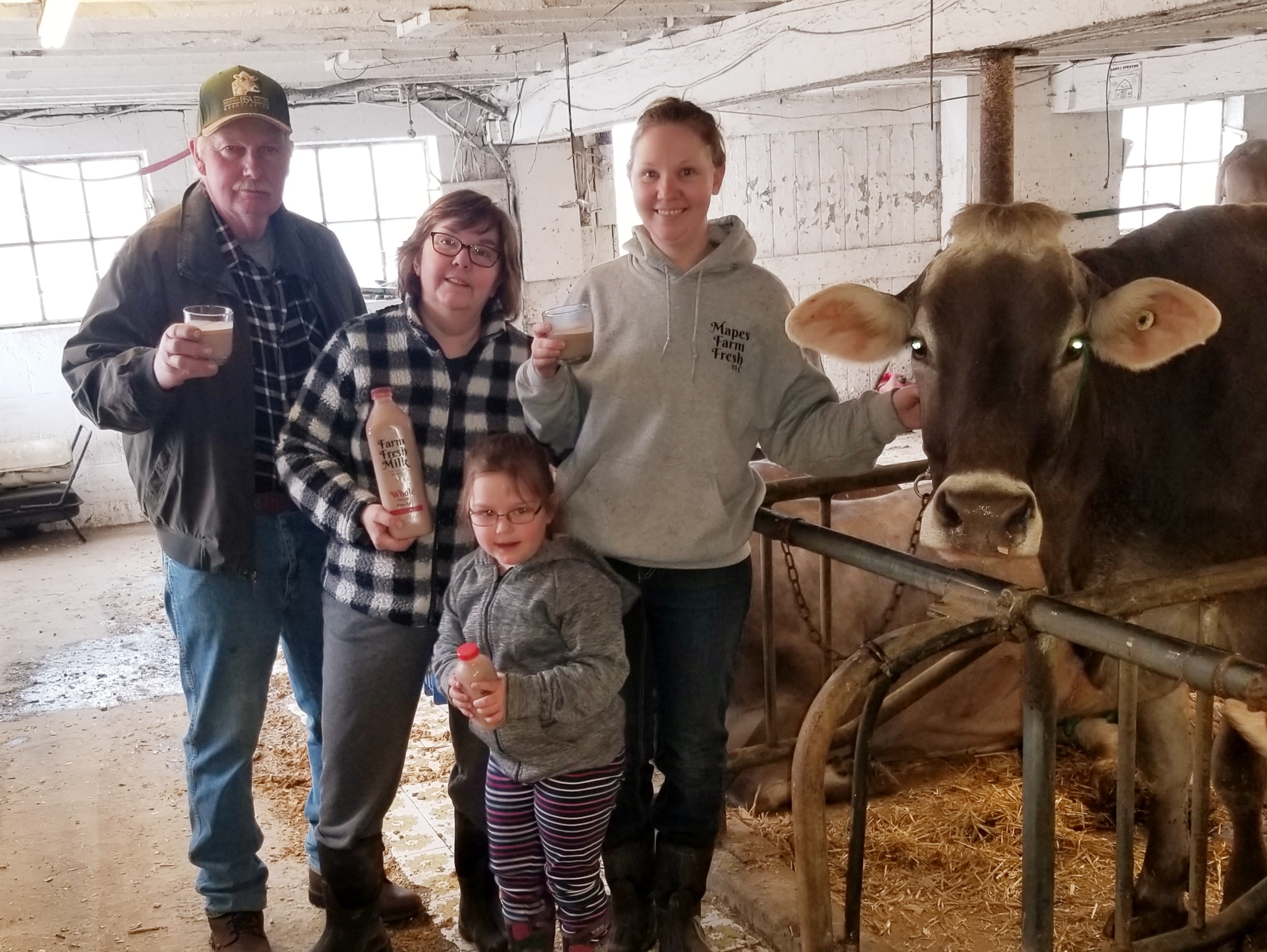Several members of a dairy family hold bottles of milk or glasses of chocolate milk while standing next to a cow.
