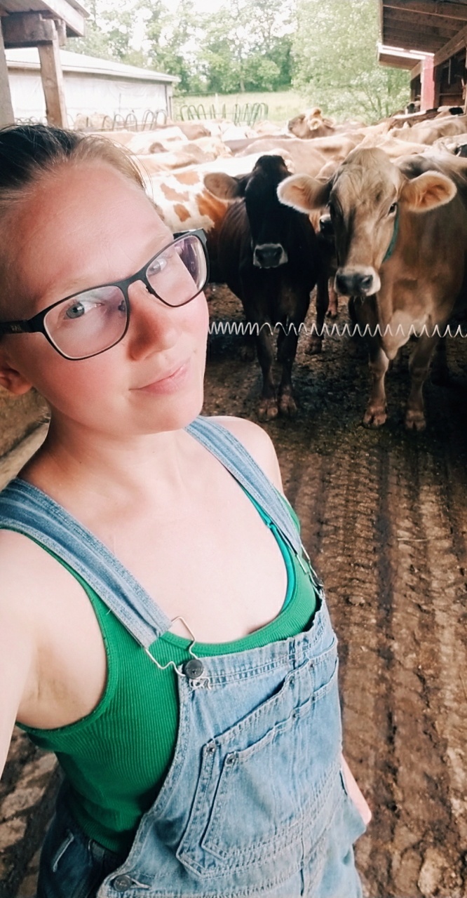A selfie of a dairy farm girl and a group of dairy cows on a farm.