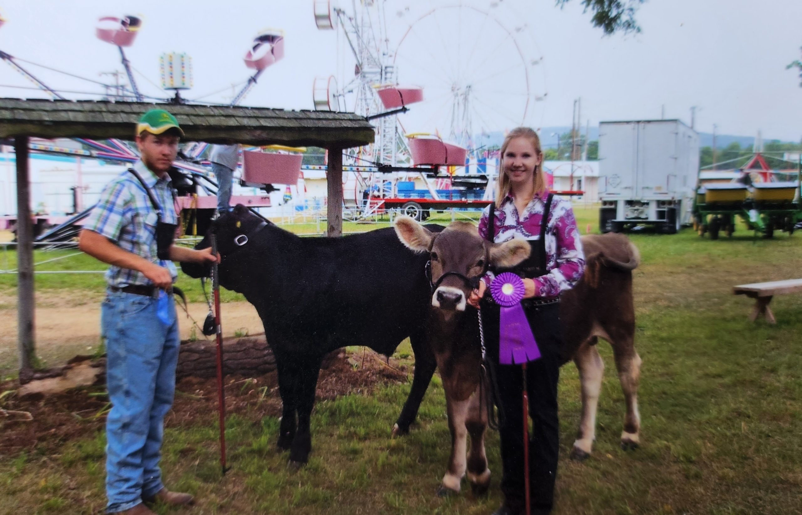 A girl holding a purple ribbon next to two cows and a boy at a fair.