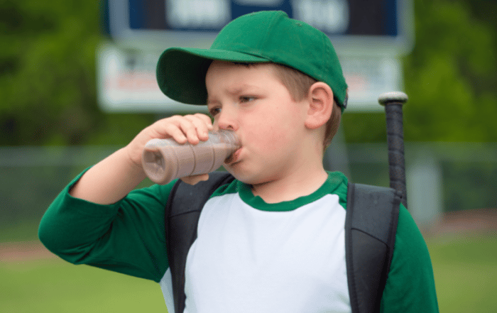 Young boy in a baseball uniform enjoying the benefits of chocolate milk after his game
