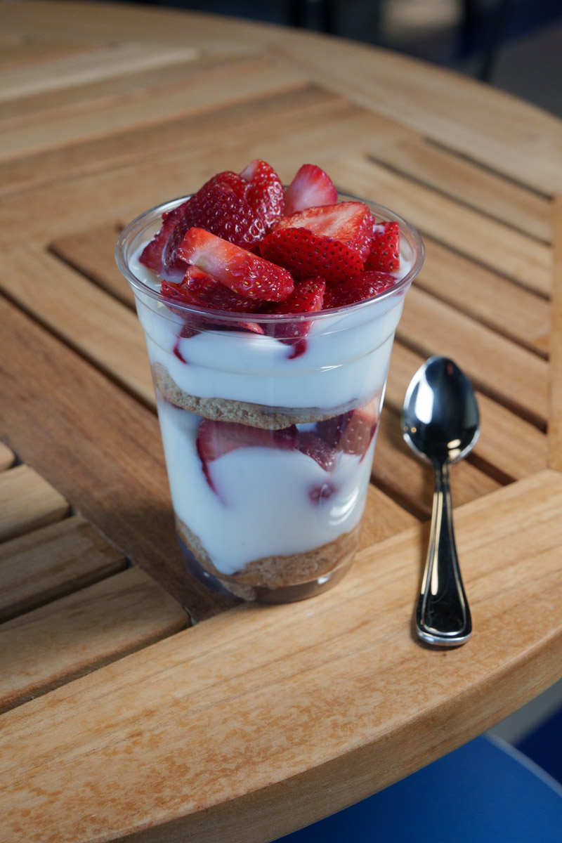 A fruit and yogurt parfait on a table next to a spoon.