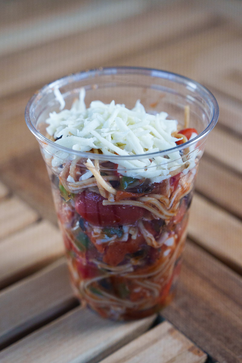 A pizza salad inside of a cup that is on a table.