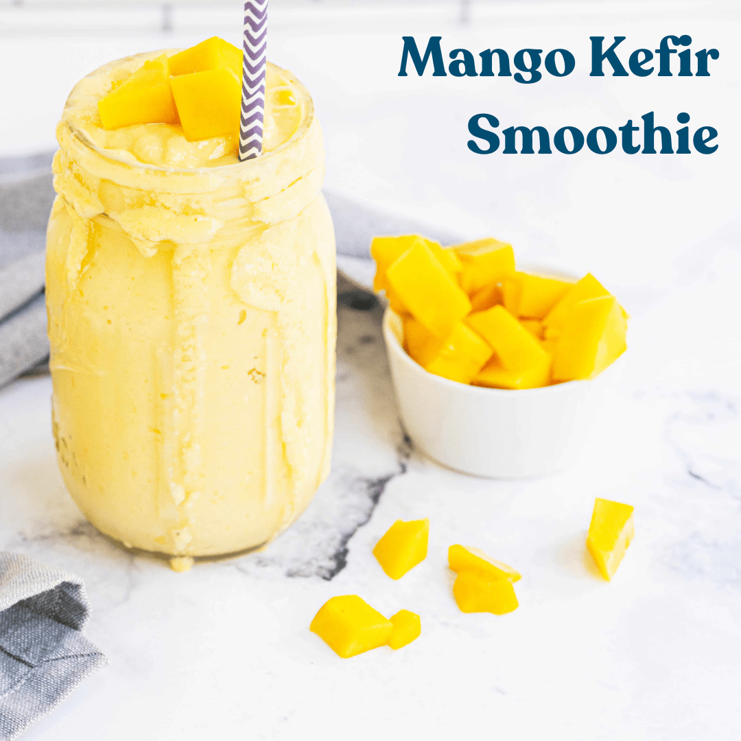 Crystal Jar filled with Mango Kefir Smoothie, with mango topping, served with a plastic straw on a white marble table and a rounded small bowl filled with mango.
