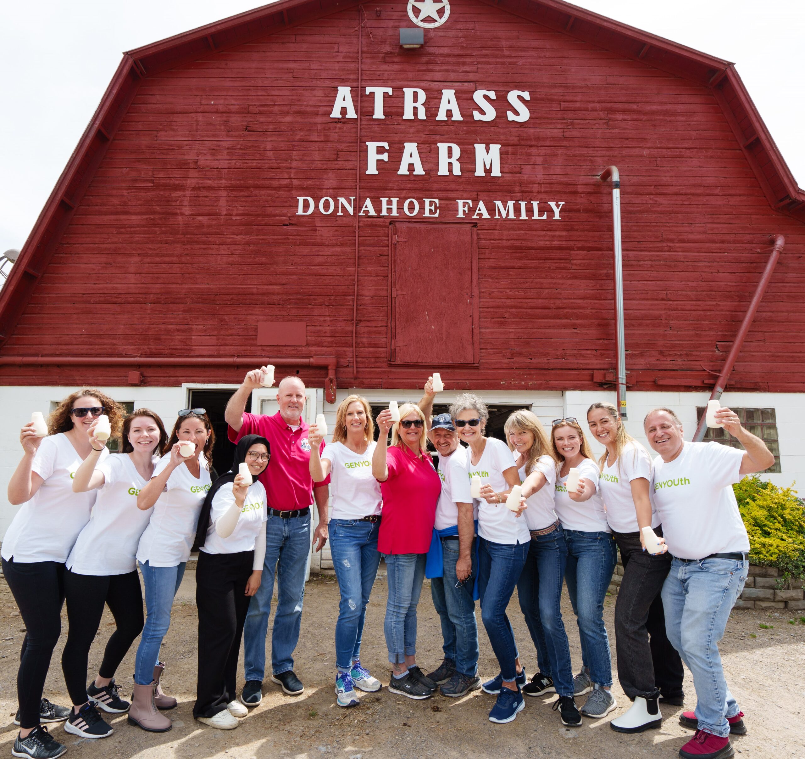 A group of people in front of a red barn, each holding a bottle of milk.