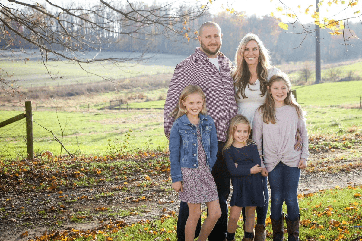 A farm couple with their three daughters in a field full of orange leaves due to the arrival of autumn.