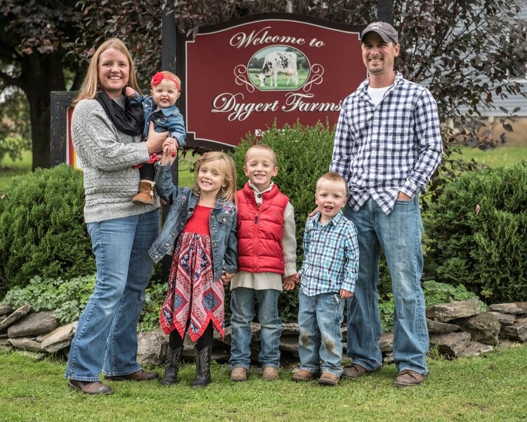 The members of the Dygert family standing and smiling in front of a sign for their farm.