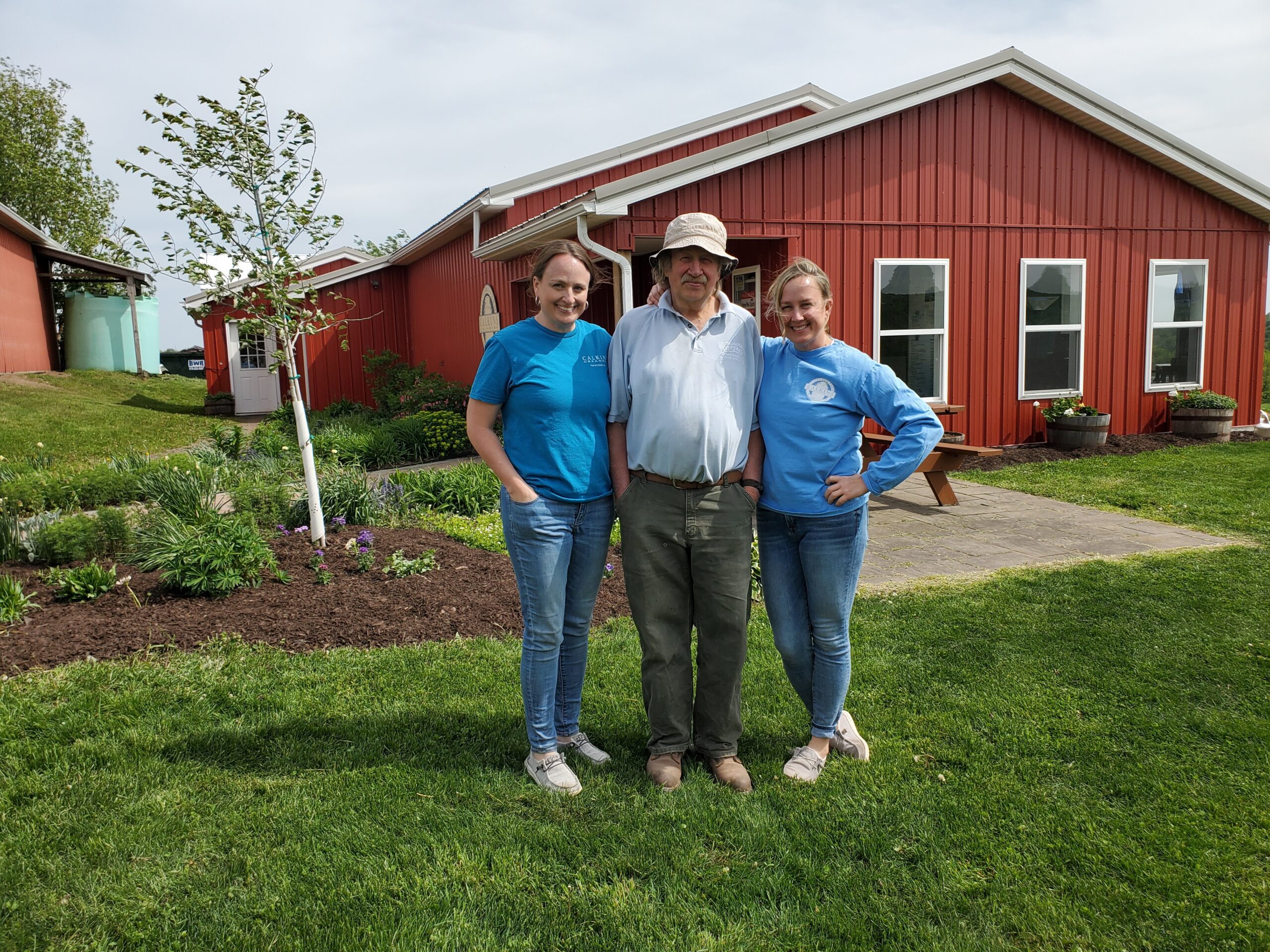 A family of dairy farmers dressed in blue t-shirts standing in a garden in front of a red barn.