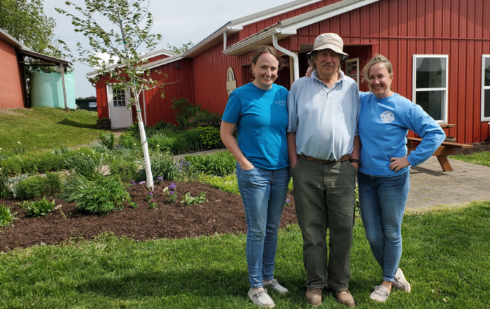 A family of dairy farmers dressed in blue t-shirts standing in a garden in front of a red barn.