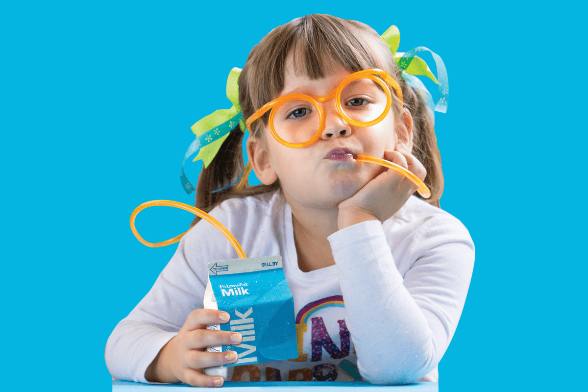 A girl wearing yellow glasses that double as a straw, connected to a bottle of milk.