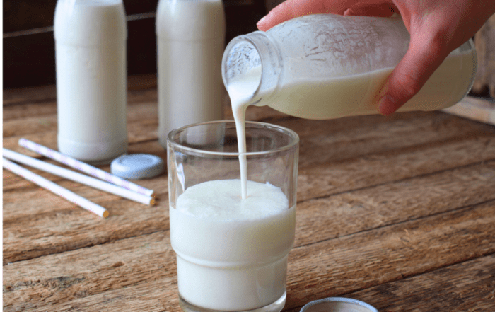 A bottle of kefir milk poured into a glass, next to a couple of glass milk bottles and spiral straws.