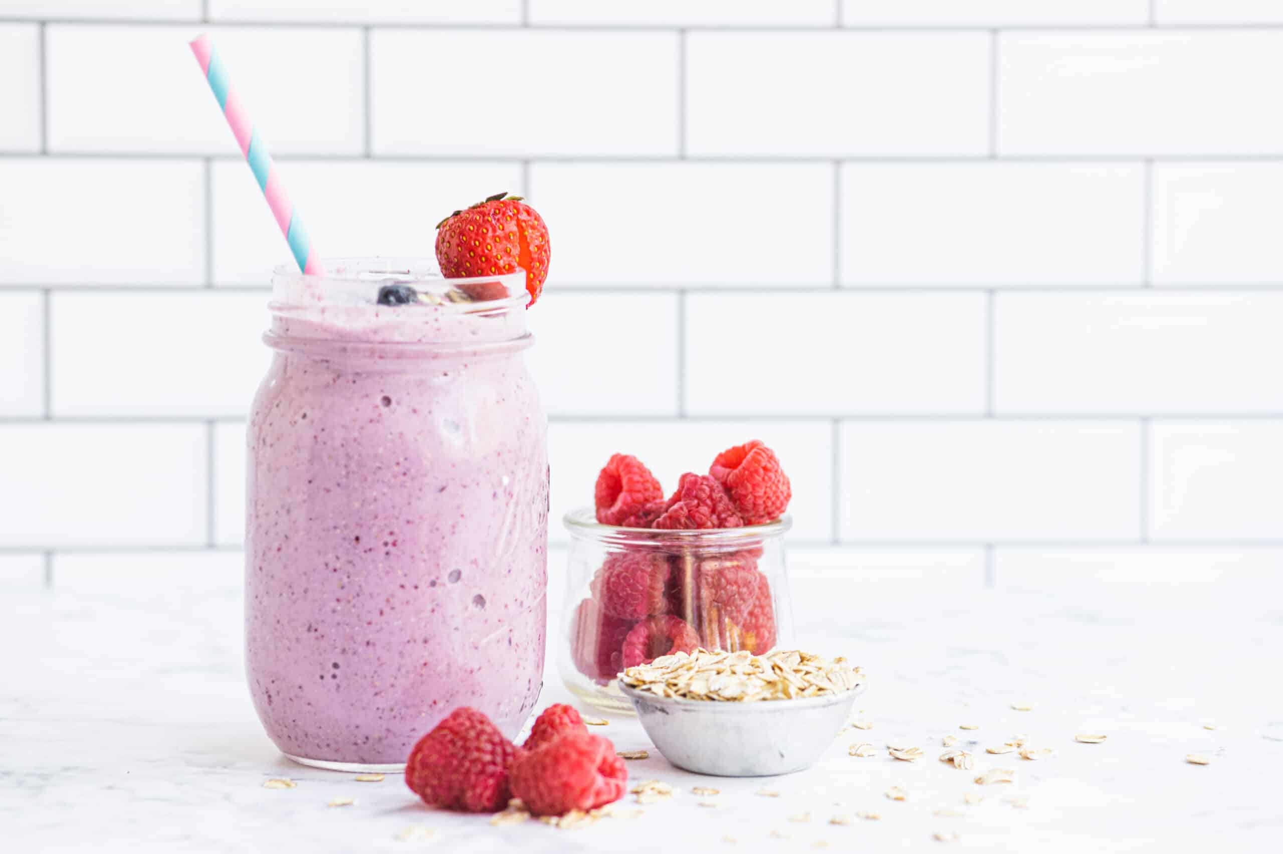 A fruit smoothie topped with berries while a small bowl of oats rests next to it.